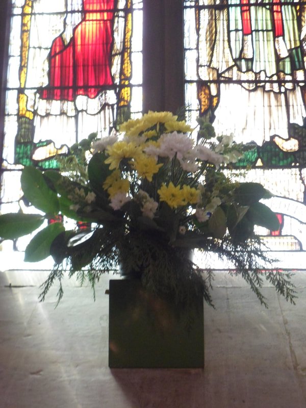 A flower arrangement in front of a stained glass window at St Barnabas